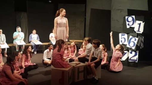 A group of young people stand on a stage acting
