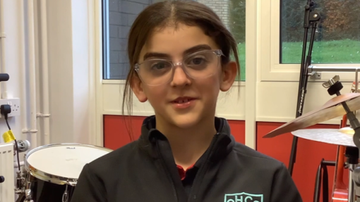 A young girl is sitting in a chair with a drum kit behind her