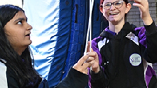 Two pupils concentrating, looking up as they balance a plate on sticks 