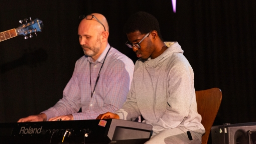 A teacher and a student are sitting together, playing piano.