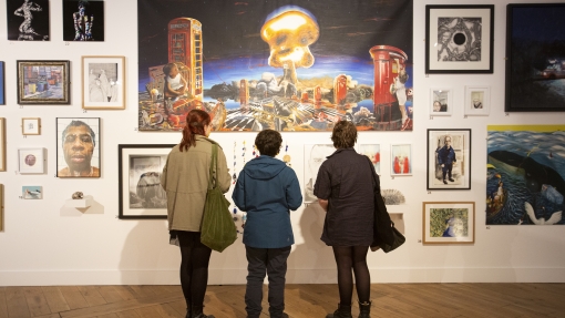 Three people with their backs to camera, are looking at art work on display in a gallery.