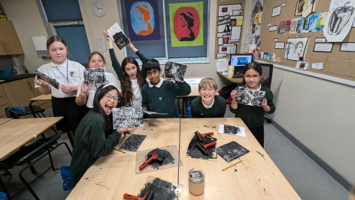 A group of pupils at a desk holding up prints