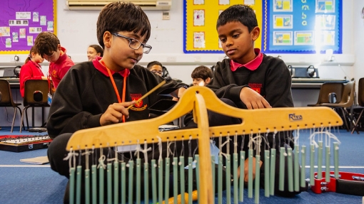 Two children are sitting on the floor in a classroom playing a musical instrument