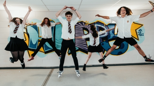 Five students jumping in front of art on wall