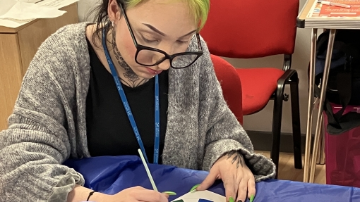 Person with green and black hair paints a colour wheel at a table with art supplies