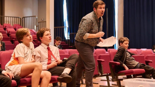 Three students are sitting down and a teacher is standing up looking off camera