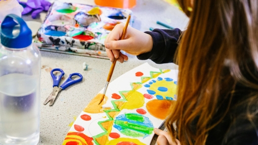 A child paints bright shapes on paper, with art supplies on the table