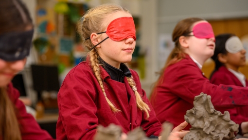 Students in red smocks shaping clay sculptures in an art classroom.