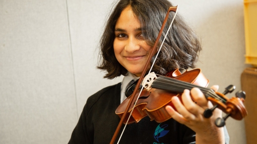 A school pupil playing the violin and looking at the camera. 