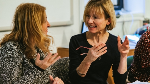 Two female adults talking at a desk, one holding a pen