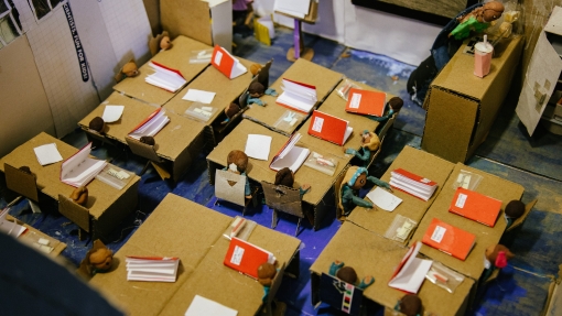 A small model classroom, made using carboard for school desks and people out of modelling clay. 