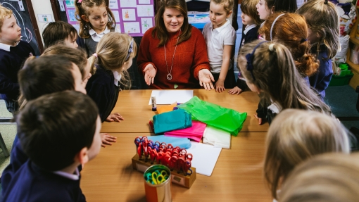 A group of children crowd around a table full of colourful paper