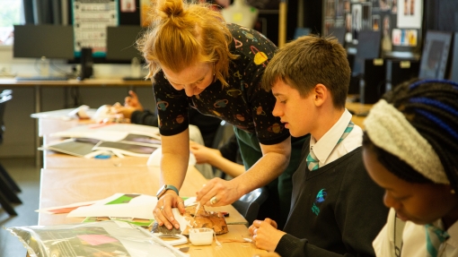 A teacher and pupil sit on a desk demonstrating how to draw.