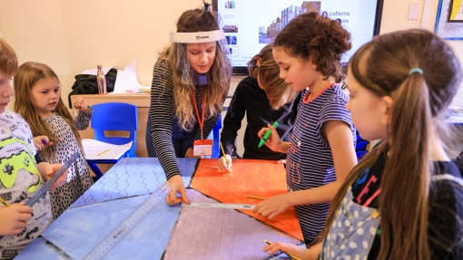 Three children sit around a table with paper hats on 