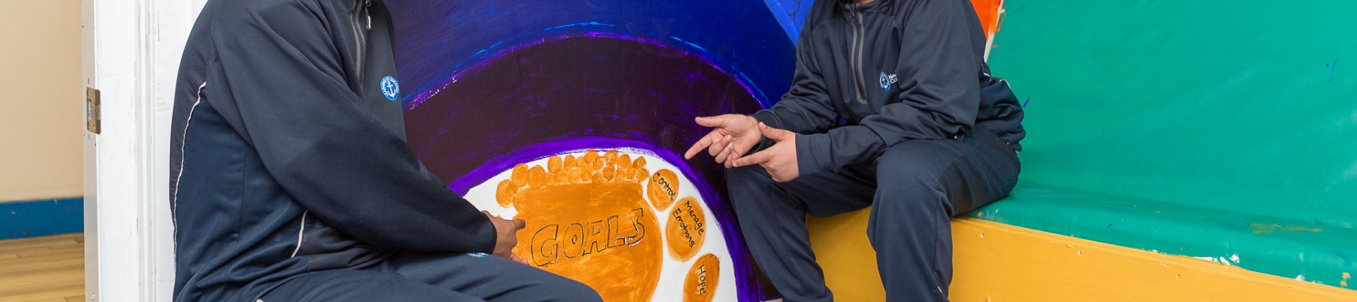 Two students sitting in front of a rainbow painted on a wall that says equality 