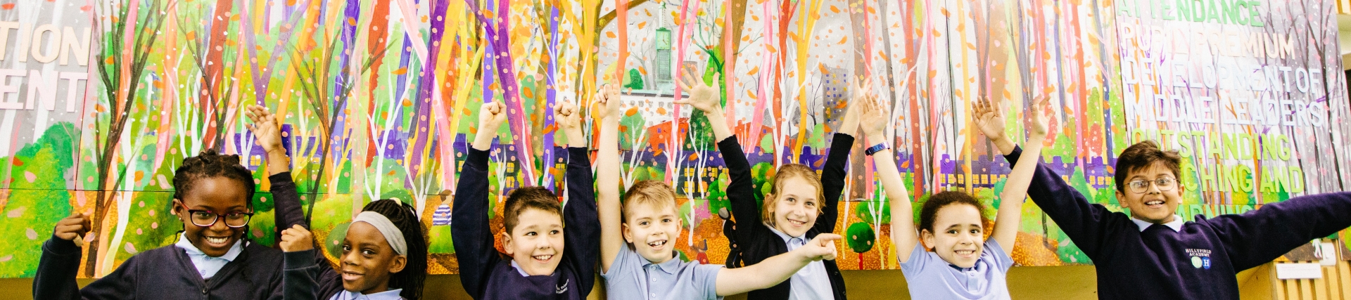 Young pupils standing in front of a colourful wall mural with their hands in the air 