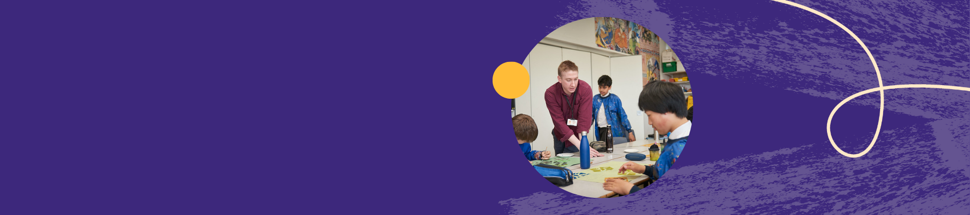 Teacher and students engaged in a classroom art activity around a table, with colorful artwork and supplies in the background.