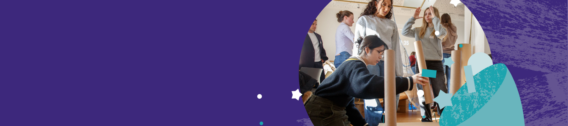 Group of people engaged in a hands-on creative activity indoors, building structures with cardboard tubes and blue blocks, with others standing and observing in the background. The scene is partially framed by a purple graphic design element.