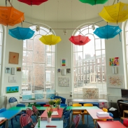 A classroom with large bay windows and colourful displays on the wall and umbrellas hanging from the ceiling 