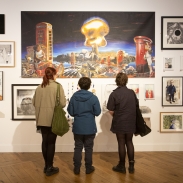 Three people with their backs to camera, are looking at art work on display in a gallery.