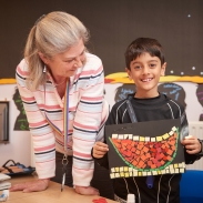 A pupil is holding up their art work and a teacher is next to him smiling. 