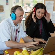 Two teachers wearing headphones looking at a laptop