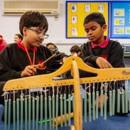 Two children are sitting on the floor in a classroom playing a musical instrument