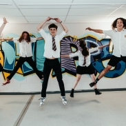 Five students jumping in front of art on wall