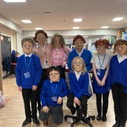 Seven children in blue sweaters and white shirts, wearing masks in a classroom 