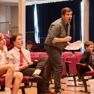 Three students are sitting down and a teacher is standing up looking off camera