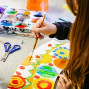 A child paints bright shapes on paper, with art supplies on the table