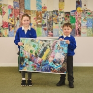 Two pupils holding up an abstract piece of art work. There is also a wall display behind them.