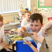 Child holding and examining a clay model in a classroom setting, with art supplies and colourful materials visible on the table. 